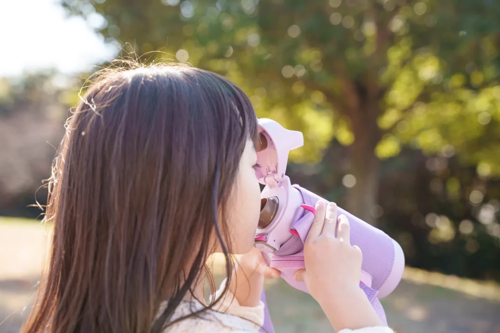 An elementary school girl drinking water from a bottle.